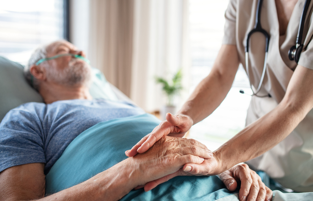 Unrecognizable female doctor examining senior man in bed in hospital.